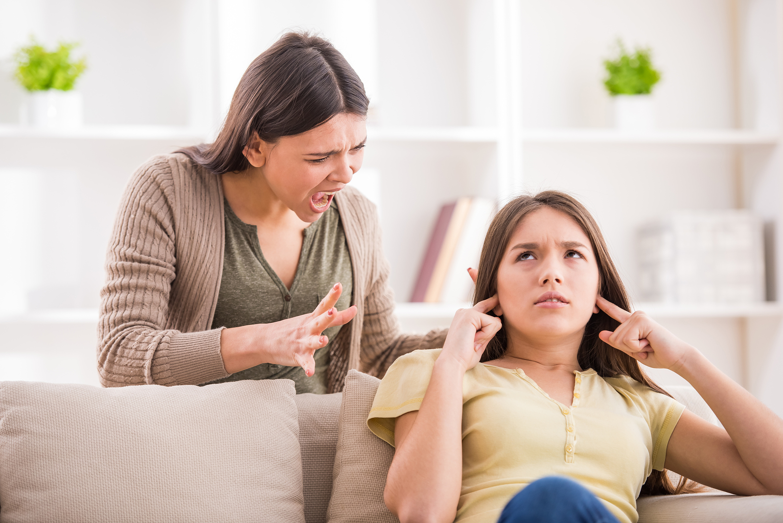 Problems between generations concept. Teen closed his ears with his hands while her mom yells at her.