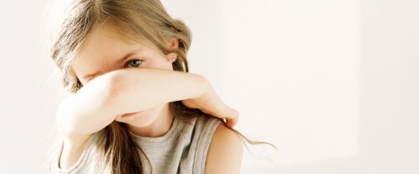 Girl with long hair anxiously holding her arm in front of her face